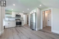 Modern kitchen featuring white shaker cabinetry, stainless steel appliances, a subway tile backsplash, and light wood-finish flooring - 
