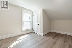 Room featuring light wood-finish flooring, white baseboards, a single window with white trim, a recessed ceiling light, and a white interior door with black hardware - 