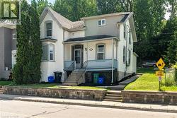 Traditional architecture featuring a covered front porch with a blue railing, bay window, and a stone retaining wall - 