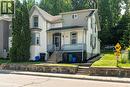Traditional architecture featuring a covered front porch with a blue railing, bay window, and a stone retaining wall - 66 Queen Street W, Cambridge, ON 