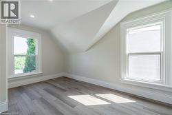 Attic room featuring sloped ceilings, two double-hung windows with white trim, wood-finish flooring, and recessed lighting - 