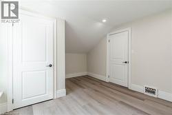 Attic space featuring wood-finish flooring, white paneled doors with matte black hardware, recessed lighting, and sloped ceilings - 