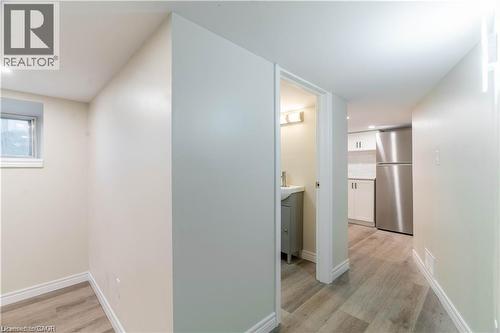 Wood-finish flooring throughout, with a window providing natural light, a compact kitchen area featuring stainless steel appliances, and a bathroom with a vanity and wall-mounted light fixture - 66 Queen Street W, Cambridge, ON 