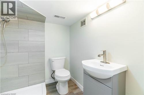 Bathroom featuring a shower with light-toned rectangular tile surround, a wall-mounted vanity with integrated sink, brushed nickel faucet, and wood-finish flooring - 66 Queen Street W, Cambridge, ON 