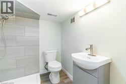 Bathroom featuring a shower with light-toned rectangular tile surround, a wall-mounted vanity with integrated sink, brushed nickel faucet, and wood-finish flooring - 