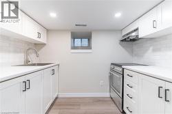 Contemporary kitchen featuring white shaker-style cabinetry with matte black hardware, a stainless steel sink with gooseneck faucet, a stainless steel range with overhead ventilation, and light-toned - 