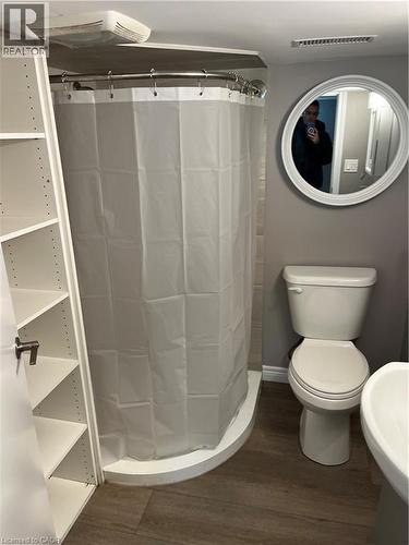 Bathroom featuring a corner shower with a curved curtain rod, a white toilet, and wood-finish flooring - 66 Queen Street W, Cambridge, ON 
