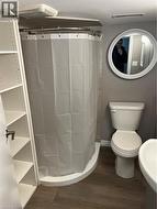 Bathroom featuring a corner shower with a curved curtain rod, a white toilet, and wood-finish flooring - 