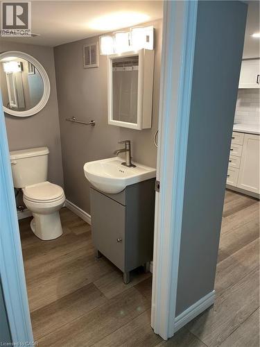 Powder room featuring a pedestal sink with a contemporary faucet, medicine cabinet with mirrored door, and a round wall mirror - 66 Queen Street W, Cambridge, ON 