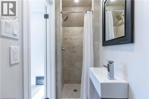 Contemporary bathroom featuring a wall-mounted rectangular sink, dark framed mirror, and a tiled shower with a rainfall showerhead - 66 Queen Street W, Cambridge, ON 