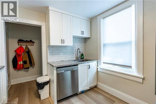 Compact kitchenette featuring white shaker-style cabinetry, a stainless steel dishwasher, and a sink with a gooseneck faucet - 66 Queen Street W, Cambridge, ON 