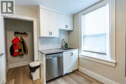 Compact kitchenette featuring white shaker-style cabinetry, a stainless steel dishwasher, and a sink with a gooseneck faucet - 