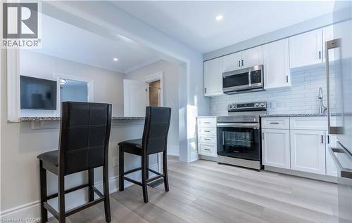 Modern kitchen featuring white cabinetry, stainless steel appliances, light-toned wood-finish flooring, a white subway tile backsplash, and a pass-through with a stone countertop - 66 Queen Street W, Cambridge, ON 