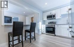 Modern kitchen featuring white cabinetry, stainless steel appliances, light-toned wood-finish flooring, a white subway tile backsplash, and a pass-through with a stone countertop - 