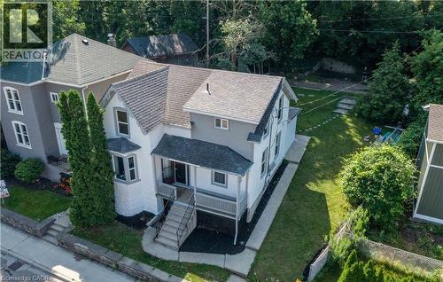 Two-story property featuring a front porch with railing, bay window, and a stone retaining wall - 66 Queen Street W, Cambridge, ON 