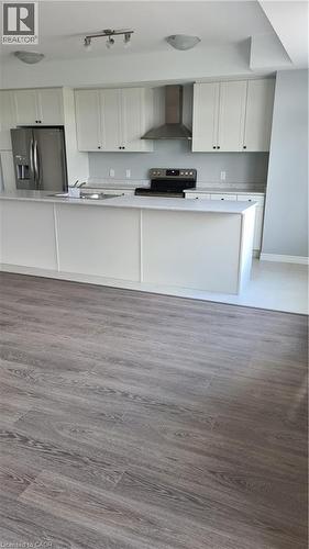 Modern kitchen featuring white cabinetry, stainless steel appliances, a center island with countertop, a tile backsplash, and wood-finish flooring - 42 Wheat Lane Unit# 42, Kitchener, ON 