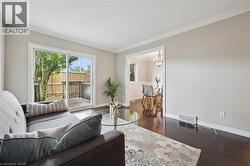 Living space featuring dark wood-finish flooring, light neutral wall tones, and white crown molding - 