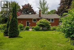 Expansive backyard featuring a manicured lawn, established landscaping, mature trees, and a brick exterior with a rear door entry - 