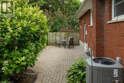 Paved patio area featuring a herringbone pattern, bordered by mature flowering shrubs and a wooden privacy fence - 