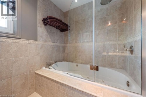 Tiled bathroom featuring a built-in tub with jets, glass shower enclosure, and a rain showerhead - 7 Thomson Road, Simcoe, ON 