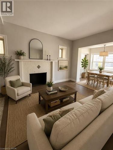 Living room featuring wood-finish flooring, a white fireplace with patterned tile surround, and neutral wall paint - 947 Main Street E, Hamilton, ON - Indoor Photo Showing Living Room