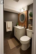 Powder room featuring a white single-sink vanity, tile flooring, a decorative mirror, exposed brick accent wall, and a single wall-mounted light fixture - 