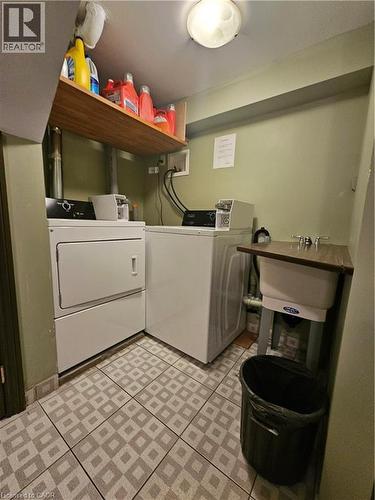 Dedicated laundry area featuring a utility sink, patterned tile flooring, and overhead wood shelving - 947 Main Street E, Hamilton, ON - Indoor Photo Showing Laundry Room