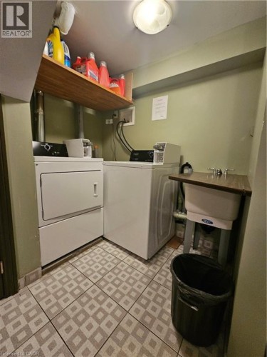 Dedicated laundry area featuring a utility sink, patterned tile flooring, and overhead wood shelving - 947 Main Street E, Hamilton, ON 