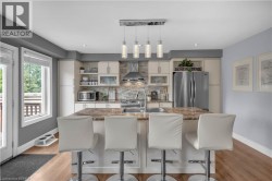 Kitchen featuring a central island with a built-in sink, stainless steel appliances, stacked stone backsplash, light wood-finish flooring, and pendant lighting - 