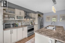 Kitchen featuring light-toned cabinetry, stainless steel appliances, a stone-look backsplash, and a central island with an undermount sink - 