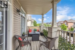 Covered outdoor balcony featuring wood-finish flooring, architectural columns, and a wall-mounted light fixture - 