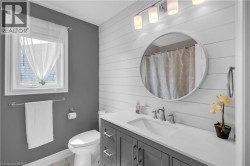 Bathroom featuring a white shiplap accent wall, a vanity with a white countertop and gray cabinetry, a rectangular undermount sink, and a circular wall mirror - 