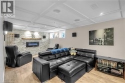 Recreation room featuring a stone accent wall with an inset electric fireplace, wood-finish flooring, and a coffered ceiling with recessed lighting - 