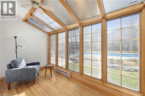 Sunroom featuring vaulted ceilings with skylights, wood-finish flooring, and large windows with integrated blinds overlooking the backyard with a pool - 277 Blackacres Boulevard, London, ON 
