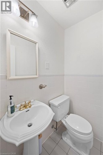 White pedestal sink featuring a brass-toned faucet, rectangular mirror, and complementary wall-mounted light fixture - 277 Blackacres Boulevard, London, ON 