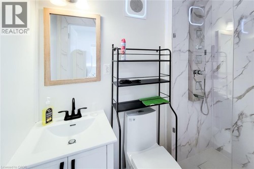 Contemporary bathroom featuring a white vanity with a black faucet, a framed mirror, a modern toilet, and a walk-in shower with marble-look wall tiling and a stainless steel shower panel - 78 Hillyard Street, Hamilton, ON 