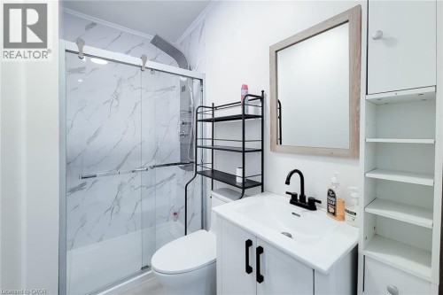 Bathroom featuring a white vanity with a black faucet, a rectangular mirror with a wood-finish frame, and white wall-mounted cabinetry with open shelving - 78 Hillyard Street, Hamilton, ON 