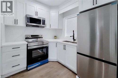 Kitchen featuring white shaker-style cabinetry, stainless steel appliances, light-toned countertops, and wood-finish flooring - 78 Hillyard Street, Hamilton, ON 