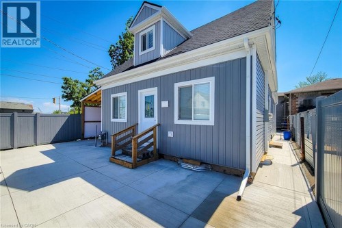 Exterior featuring vertical gray siding and white trim, concrete patio, wooden entrance stairs, and a fenced perimeter - 78 Hillyard Street, Hamilton, ON 