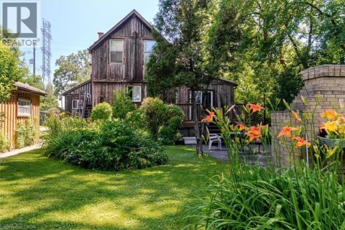 Expansive rear yard featuring a manicured lawn, lush plantings, a brick outdoor fireplace, a patio area, and a rustic wooden outbuilding - 382 Beach Boulevard, Hamilton, ON 