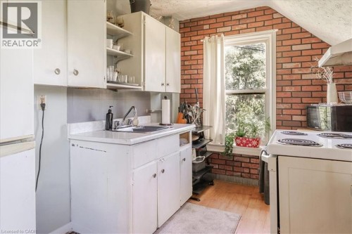Kitchen featuring, wood-finish flooring, white cabinetry, a single basin sink, and a double-hung window - 382 Beach Boulevard, Hamilton, ON 