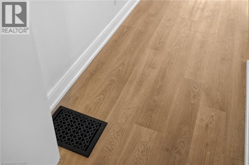 Wood-finish flooring complemented by white baseboards and a black ornate floor register - 118 Cathcart Street, Hamilton, ON 