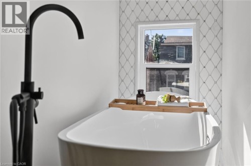Freestanding white soaking tub with a matte black floor-mounted faucet and handheld shower - 118 Cathcart Street, Hamilton, ON 