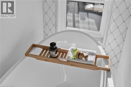 Deep soaking tub with a tiled surround featuring a geometric pattern and a single window for natural light - 118 Cathcart Street, Hamilton, ON 