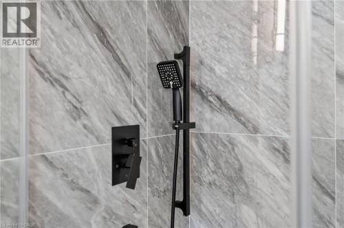 Contemporary shower with matte black fixtures, including a handheld showerhead and control panel, set against large format gray marble-look wall tiles - 118 Cathcart Street, Hamilton, ON 