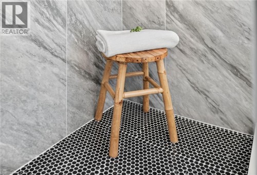 Shower enclosure featuring large format grey marble-effect wall tiles, black hexagonal mosaic floor tiling, and a contrasting white grout line - 118 Cathcart Street, Hamilton, ON 