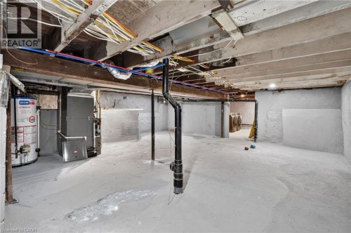 Unfinished basement featuring exposed wood joists, concrete flooring, a water heater, a furnace, and exposed plumbing and electrical conduits - 118 Cathcart Street, Hamilton, ON 