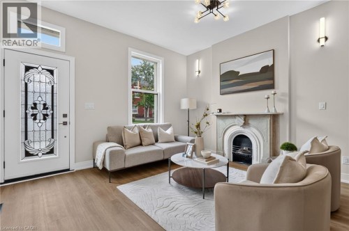 Living area featuring wood-finish flooring, a decorative fireplace with a carved mantel, and a multi-light ceiling fixture - 118 Cathcart Street, Hamilton, ON 