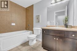 Bathroom featuring a bathtub with full-height subway tile surround, complementing floor tile, and a dark wood-finish vanity with a light countertop - 