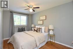 Bedroom featuring wood-finish flooring, a ceiling fan with integrated lighting, a window with horizontal blinds, and light gray painted walls - 